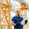 Worker in safety gear inspecting construction site with clipboard.